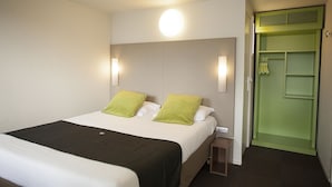 Ein Hotelzimmer mit einem Bett, zwei Kissen, einem Nachttisch, einer Wandleuchte und einer grünen Tür.