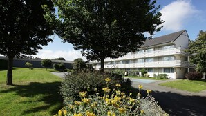 Ein zweigeschossiges Hotel mit flachem Dach, großen Fenstern und einem gepflegten Rasen mit gelben Blumen.