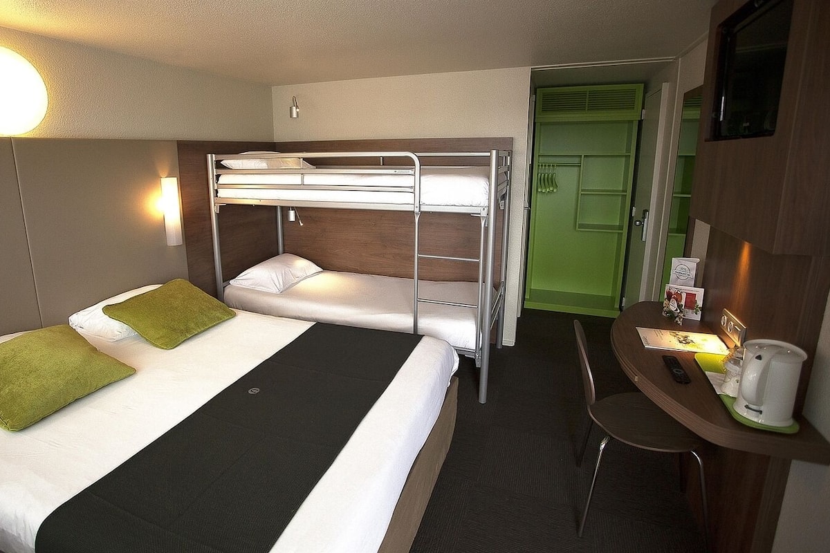A compact hotel room with bunk beds, a desk with a coffee maker, and a green door.