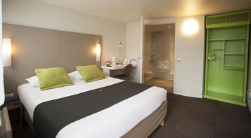 Habitación de hotel con una cama grande, una mesita de noche con lámpara, un armario verde y zona de ducha.