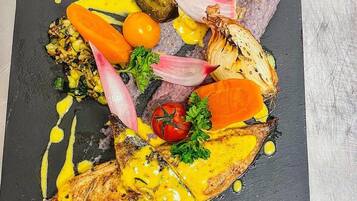 Una taula de presentació de pissarra negra amb diversos aliments, com un tros de peix a la planxa, verdures i una salsa.