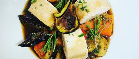 A white plate with a dish of fish, vegetables, and herbs.