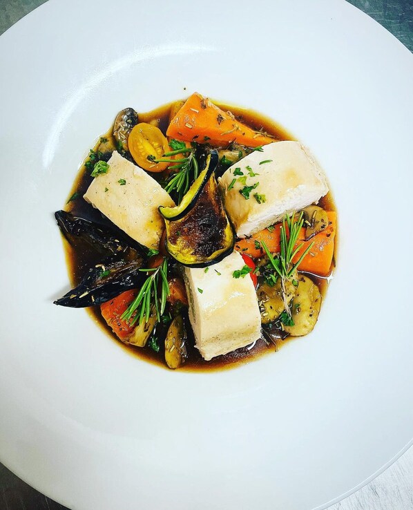 Un plato blanco con un guiso de pescado, verduras y hierbas.