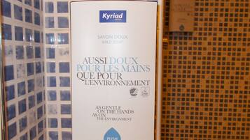 A hotel soap dispenser with the text "Kyriad Hotel" and "Aussi doux pour les mains que pour l'environnement" indicating it's gentle on hands and the environment.