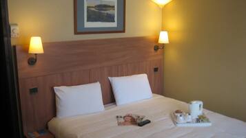 A hotel room with a bed, two bedside lamps, a framed picture on the wall, and a tray with a coffee pot and other items.