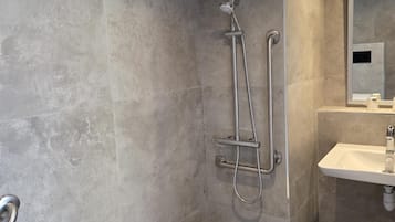 Um banheiro moderno com chuveiro, um banquinho branco pequeno, pia e espelho.