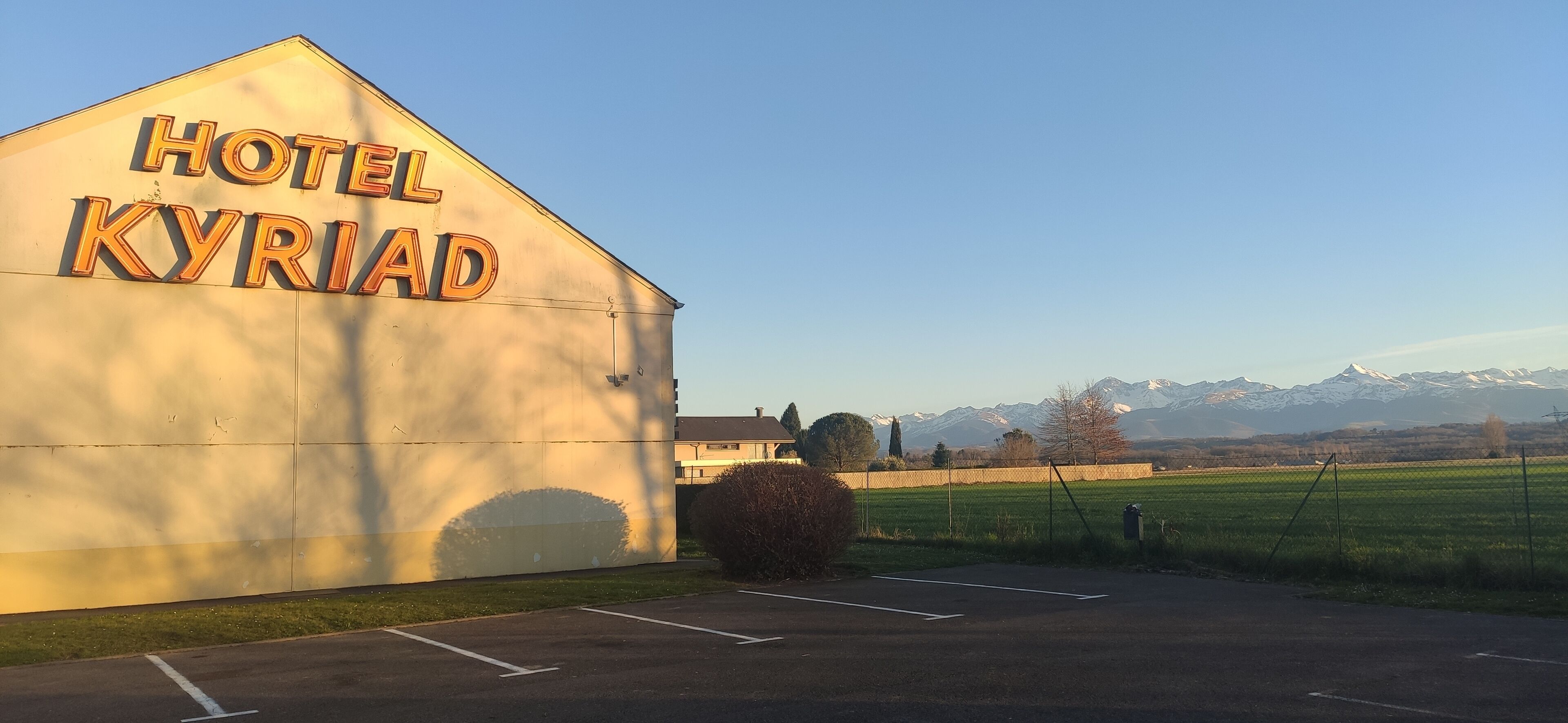 Un edificio con un letrero que dice "HOTEL KYRIAD" y un estacionamiento enfrente.