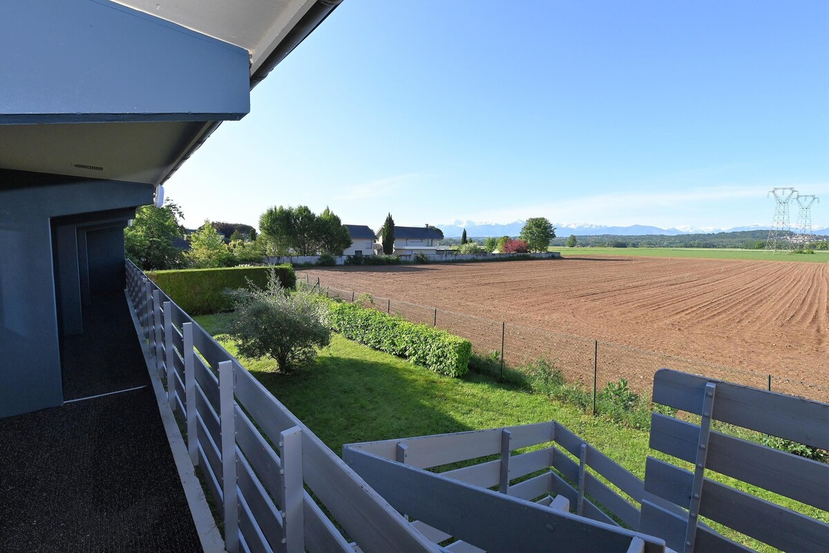 Un balcón con vista a un campo cultivado, una valla blanca y una casa distante.