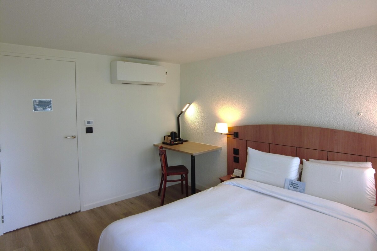 Una habitación de hotel con una cama, un escritorio, una silla, una lámpara y un equipo de aire acondicionado.