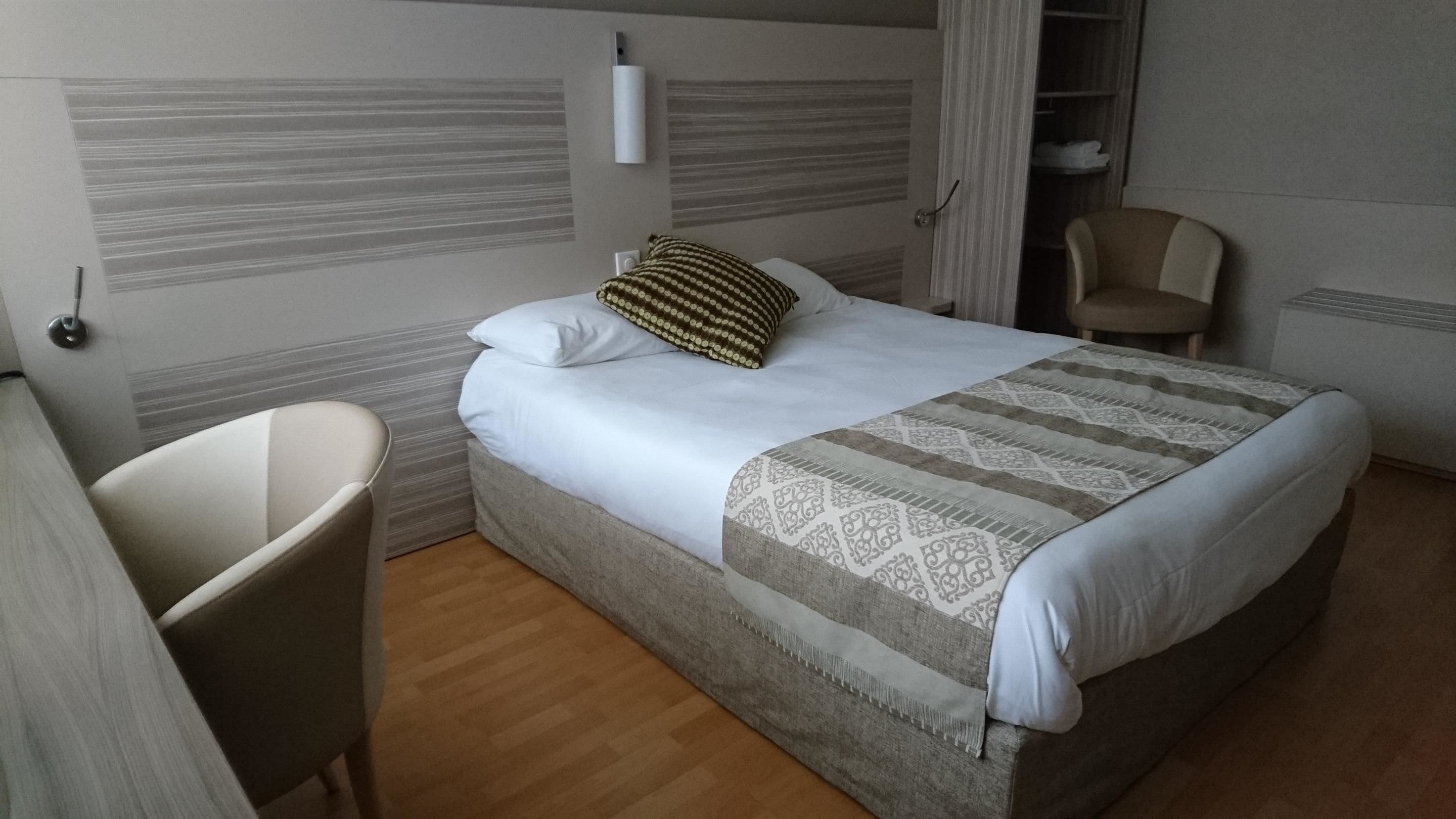 A hotel room with a bed, a chair, and a wardrobe.