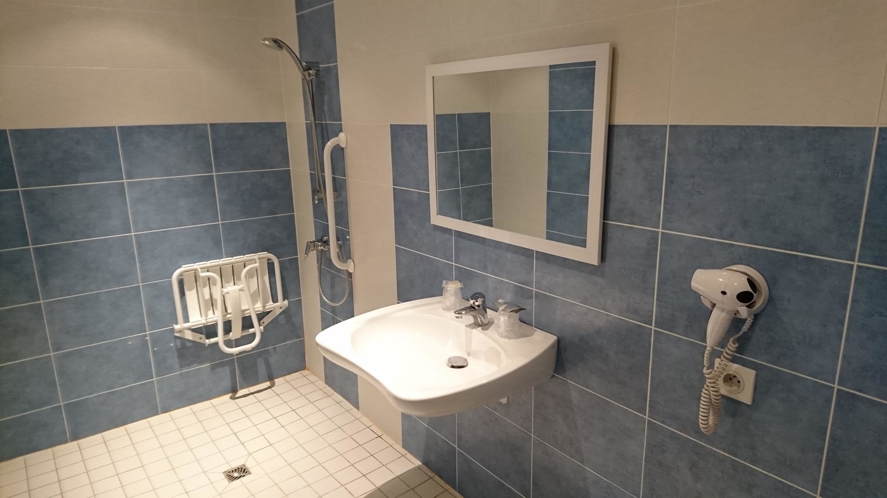 A bathroom with a shower, a sink, a mirror, and a hairdryer.
