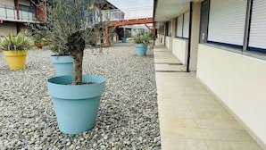A building with a covered walkway, potted plants, and a gravel ground.