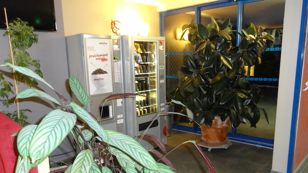 A vending machine with a sign, a potted plant, and a glass door entrance. - Hotel Kyriad Toulouse Sud - Roques (Roques)