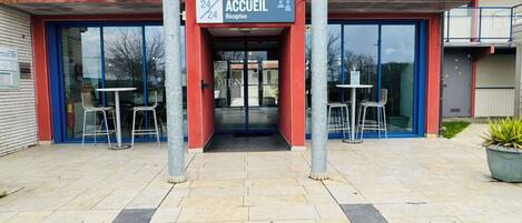 A hotel entrance with a reception desk, glass doors, and outdoor seating area.