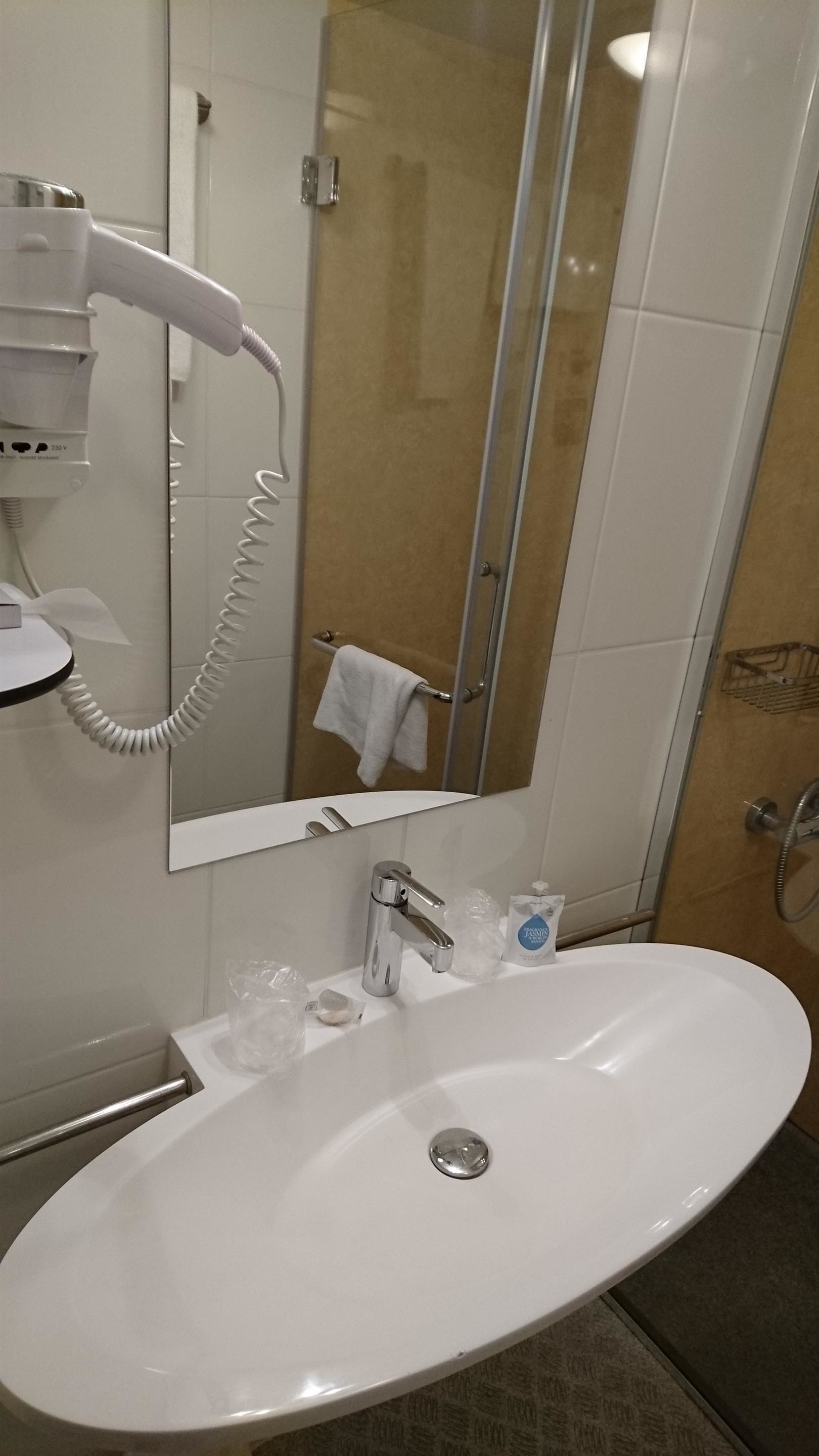 Un baño con un lavabo blanco, un secador de pelo de mano, un espejo y una puerta de ducha de cristal.
