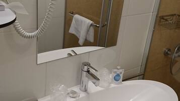 Un baño con un lavabo blanco, un secador de pelo de mano, un espejo y una puerta de ducha de cristal.