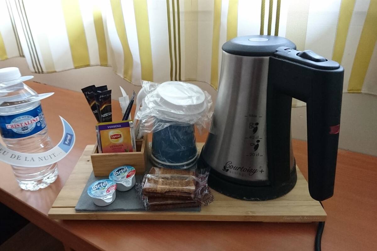 A wooden table with a bottle of water, a kettle, a box of tea, a pack of tissues, and a small container of yogurt.