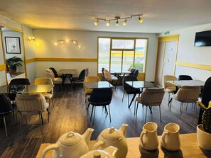 A dining area with tables and chairs, a large window, and a ceiling light fixture. - Hotel Kyriad Toulouse Sud - Roques (Roques)