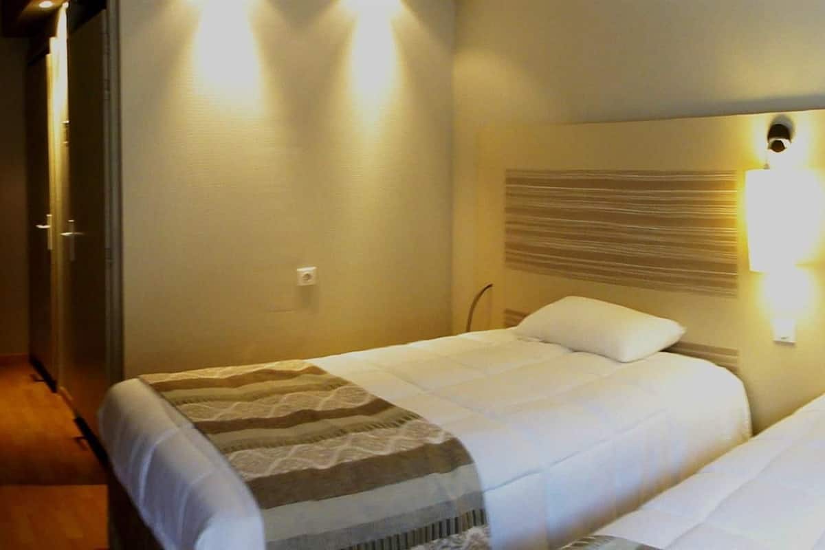 A hotel room with two beds, a TV, and a wall-mounted light fixture.
