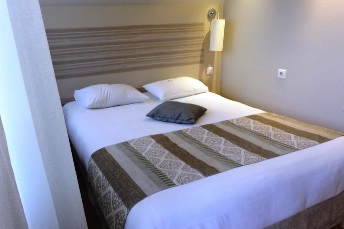 A neatly made bed with a patterned bedspread, white pillows, and a single gray pillow.