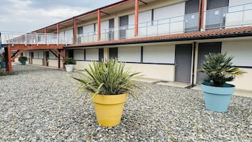 Um edifício com telhado vermelho, várias varandas e plantas em vasos no pátio.
