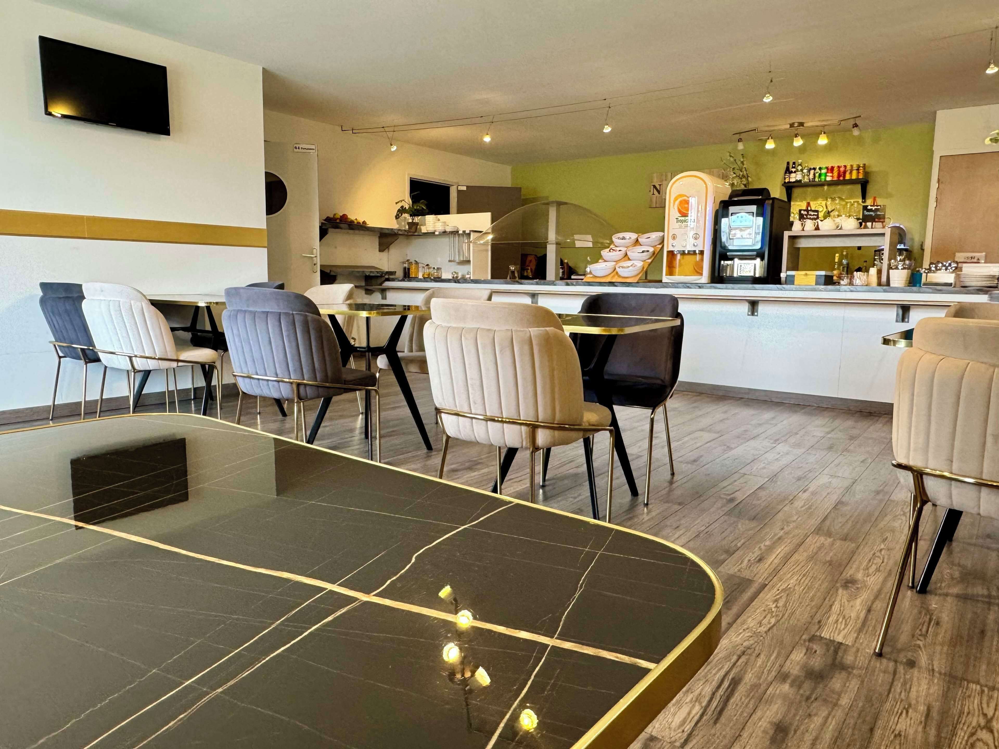 A modern dining area with a black marble table, beige upholstered chairs, and a kitchen in the background.