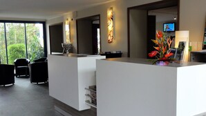 A modern reception area with a white reception desk, a large mirror, and a television mounted on the wall.