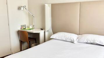 Una habitación de hotel con cama, escritorio, silla, lámpara y armario.
