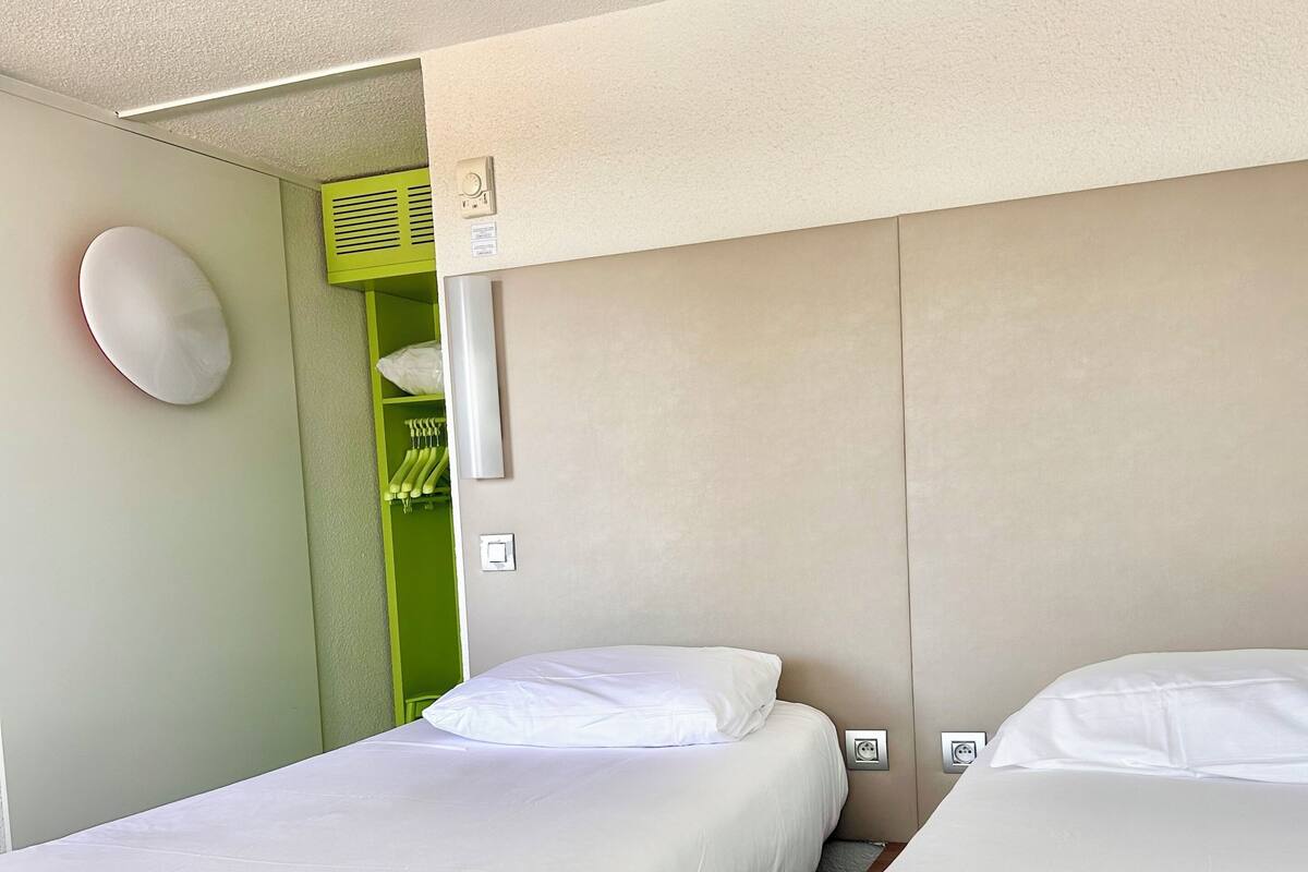 Une chambre d’hôtel avec deux lits simples, un mur vert et un plafond blanc.