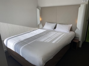 Cama bem arrumada com lençóis brancos, cabeceira e abajures.