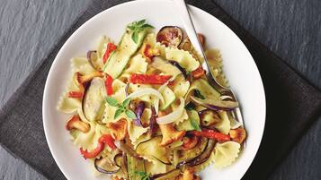 Een kom pasta met groenten op een donkere ondergrond.