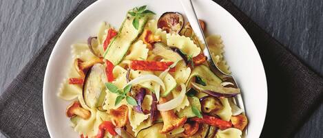 A bowl of pasta with vegetables on a dark surface.