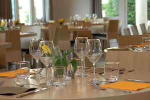 Un comedor con mesas dispuestas para el servicio, cristalería transparente y una planta en maceta sobre la mesa.