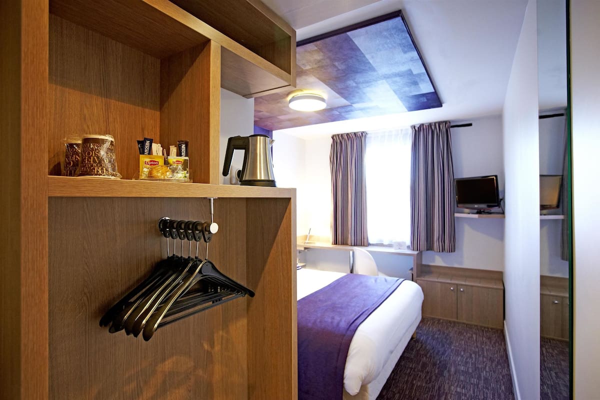 Een hotelkamer met een bed, een televisie, een bureau en een houten garderobe.