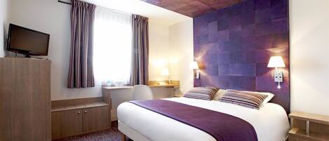 Una habitación de hotel con una cama grande, un escritorio, una televisión y un ventanal con cortinas.