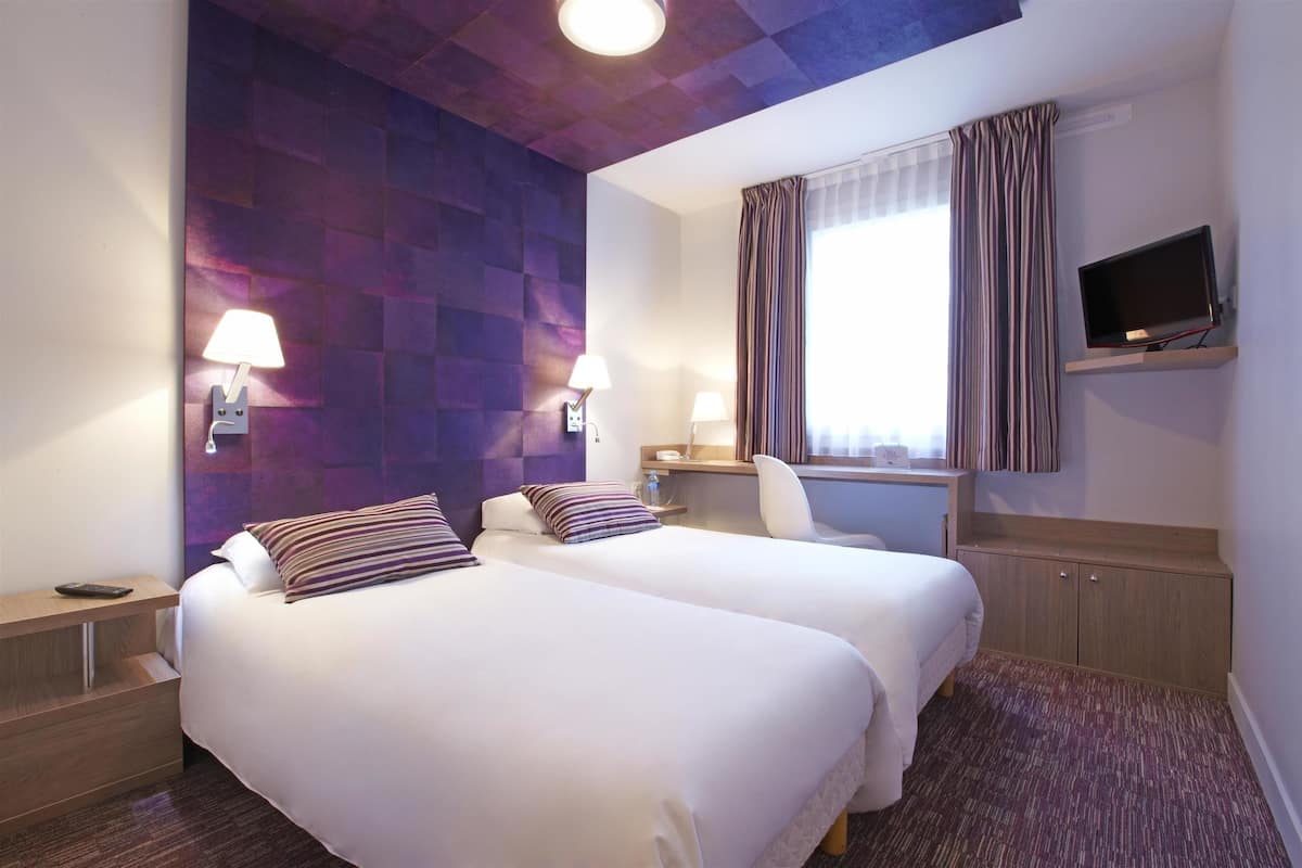 Een hotelkamer met twee bedden, een bureau, een televisie en een raam met gordijnen.