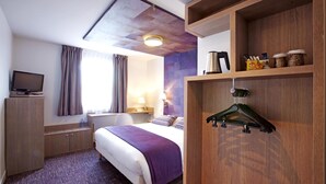 Une chambre d’hôtel équipée d’un lit, d’un bureau, d’une télévision, d’une armoire et d’une étagère avec des en-cas.