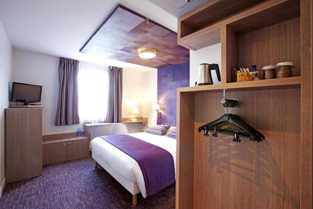 Habitación de hotel con cama, escritorio, televisión, armario y estante con aperitivos.