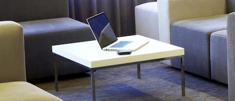 A laptop on a small white table in a hotel room with grey upholstered chairs.