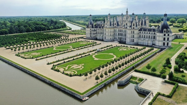 Un grand bâtiment historique doté d’un jardin à la disposition symétrique, d’un élément aquatique central et, au loin, d’une rivière.
