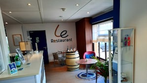 L’intérieur d’un restaurant avec un comptoir d’accueil, un tonneau en bois, une chaise rouge et une plante en pot.