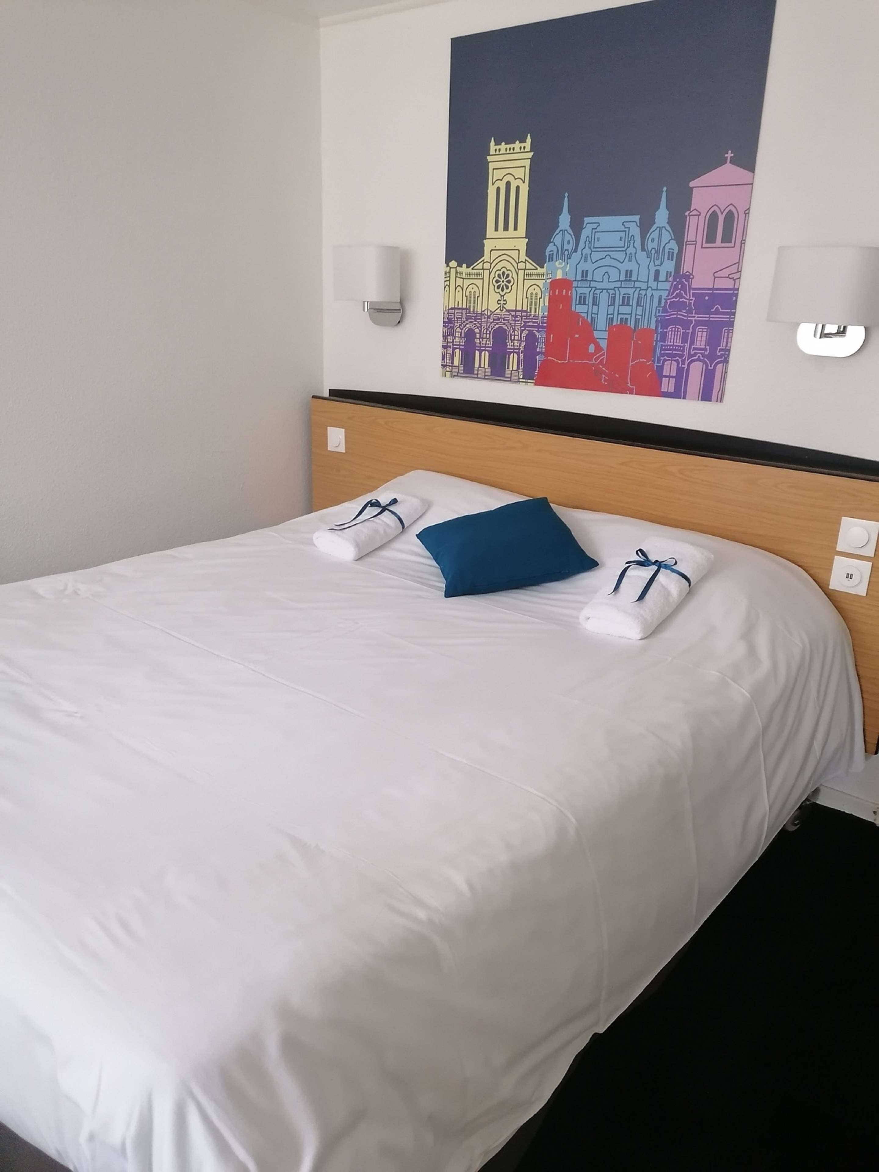Une chambre d’hôtel avec un lit bien fait, une tête de lit et une œuvre d’art accrochée au mur représentant un paysage urbain.