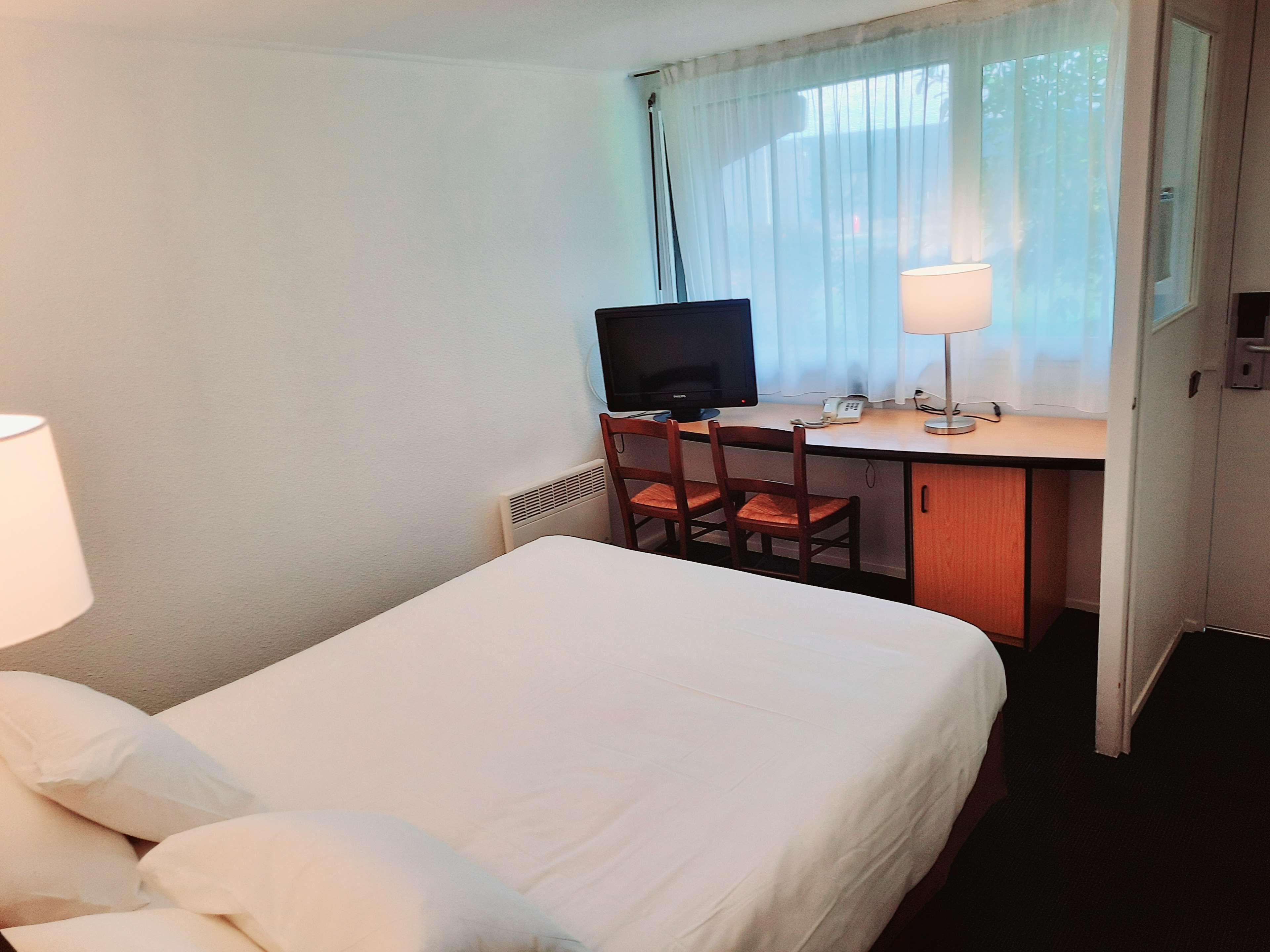 Ein Hotelzimmer mit Bett, Schreibtisch, Computer, Stuhl und Lampe.