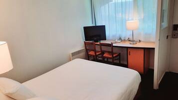 Ein Hotelzimmer mit Bett, Schreibtisch, Computer, Stuhl und Lampe.