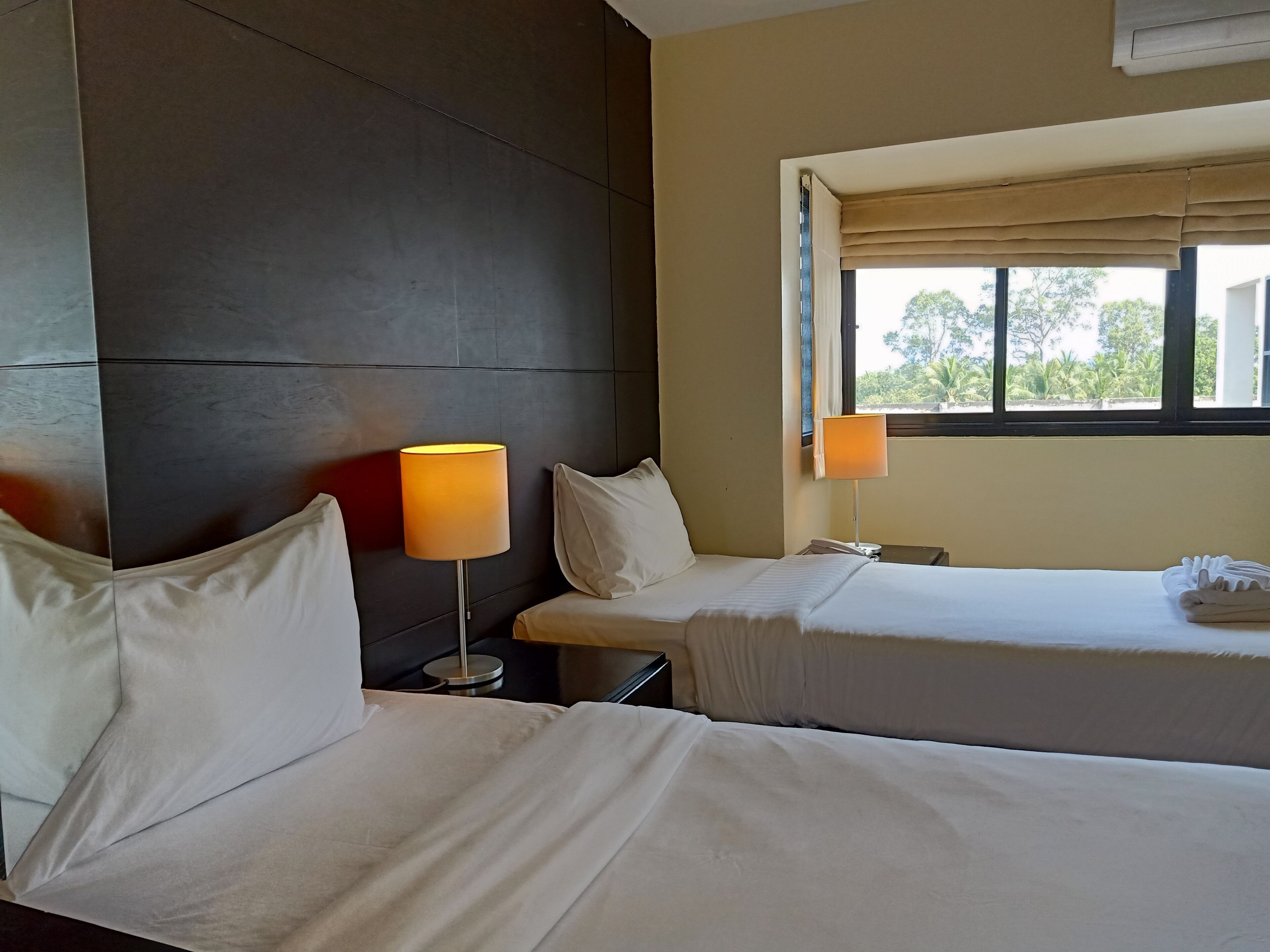A hotel room with two beds, a large window with curtains, and a wall-mounted air conditioning unit.