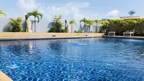 Una piscina con agua cristalina azul, rodeada de palmeras y un muro de piedra.