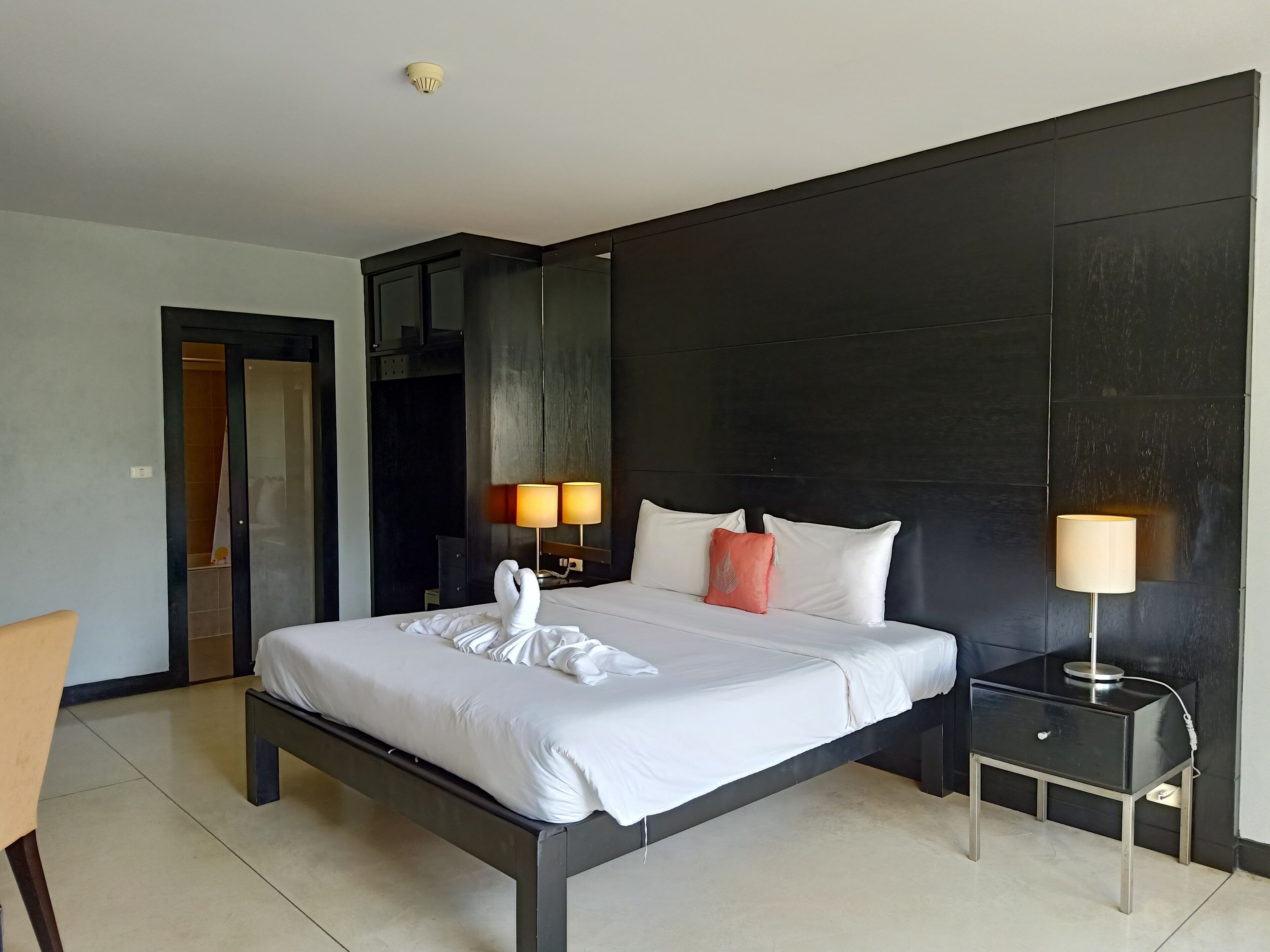 A modern hotel room with a large bed, two bedside lamps, a dark accent wall, and a small bedside table.