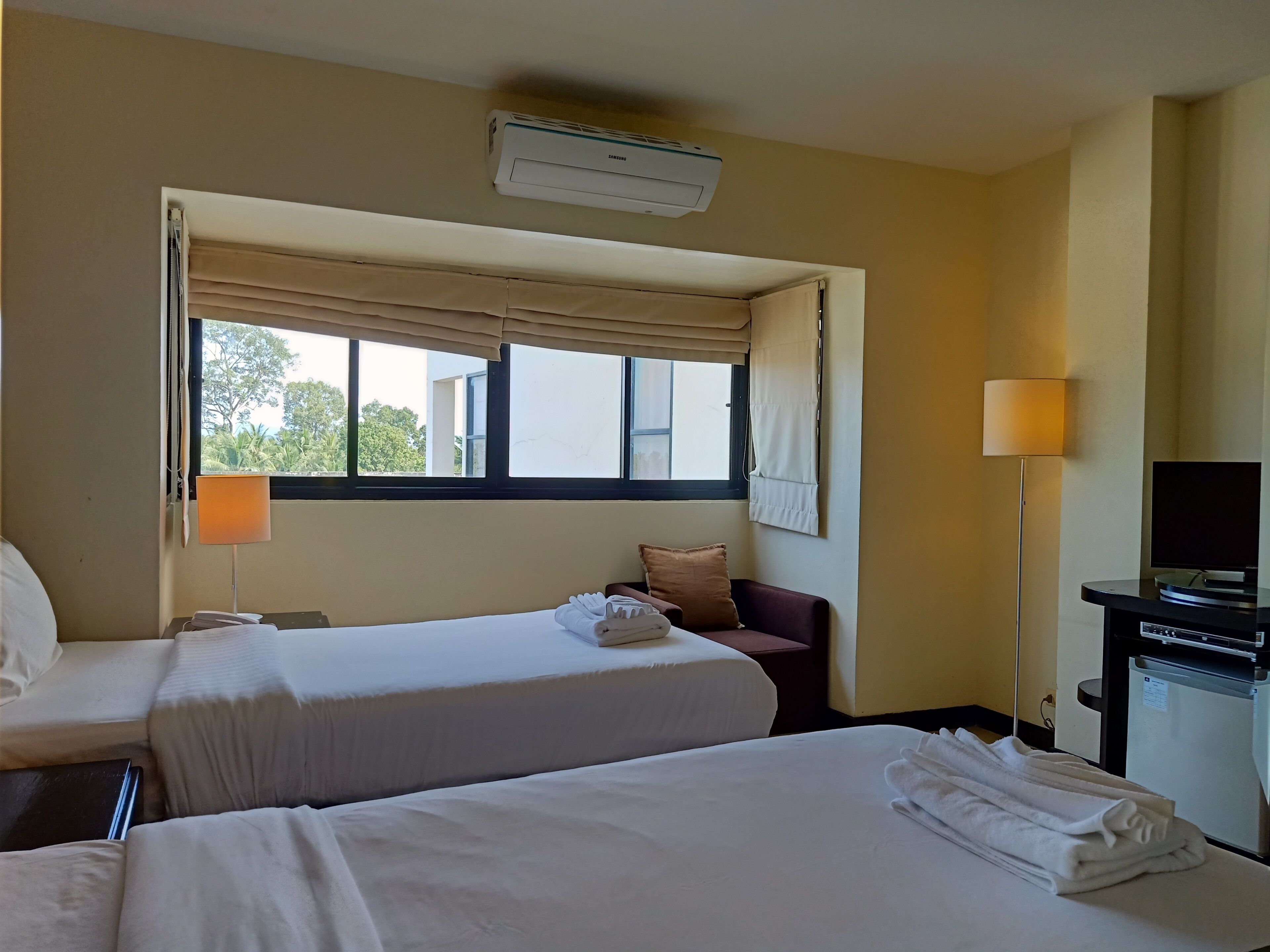 A hotel room with two beds, a TV, a desk, and a window with curtains.