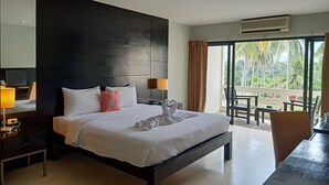 Habitación de hotel con una cama grande, televisión, escritorio y balcón con mobiliario exterior.