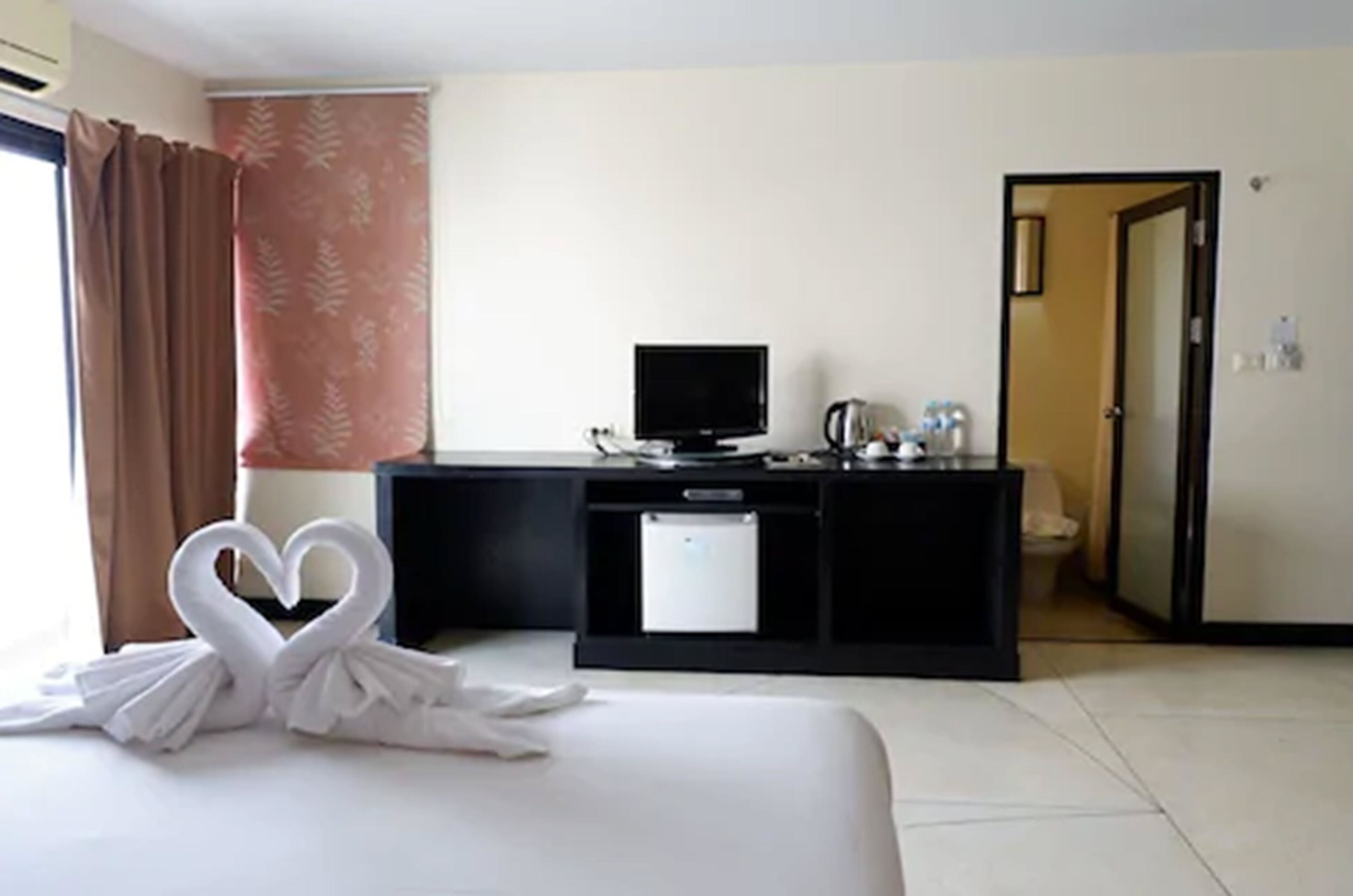 A hotel room with a bed, a desk with a computer, a TV, and a door leading to a bathroom.